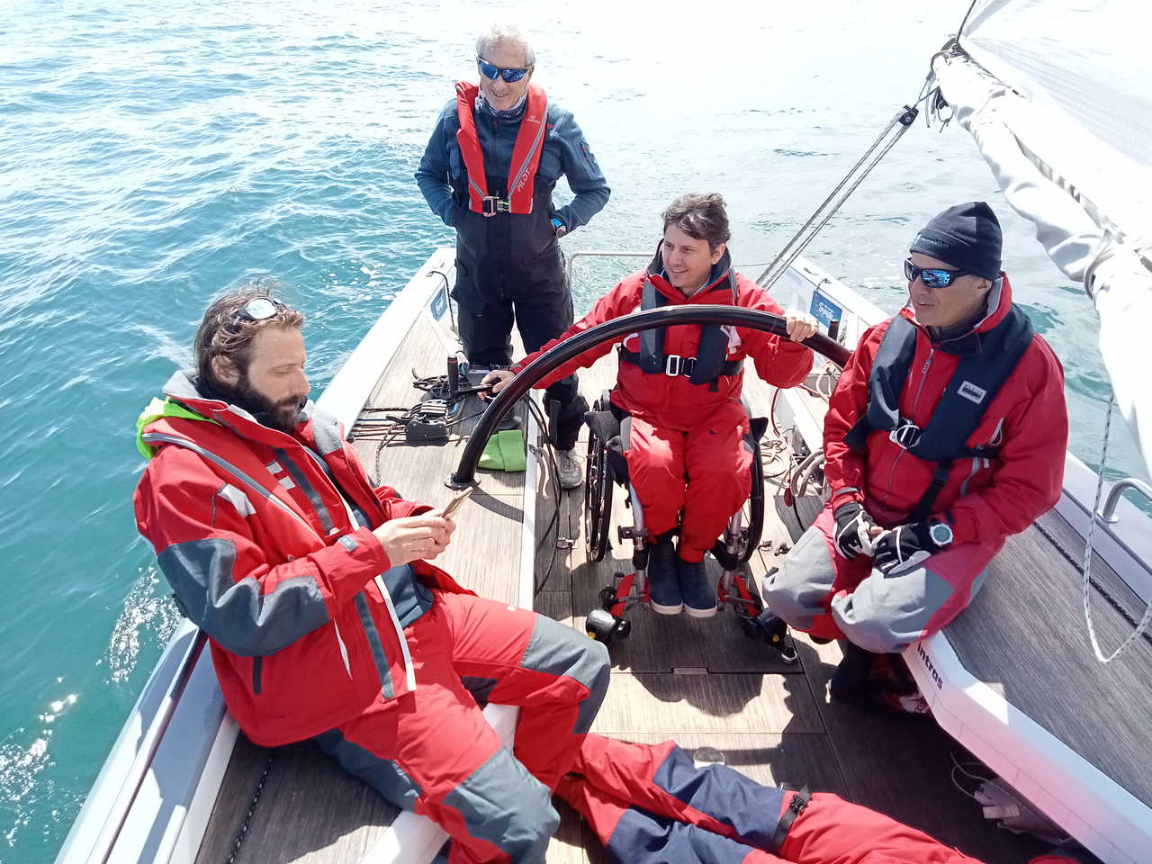 Sailing crew including a wheelchair user at the helm of a yacht at sea